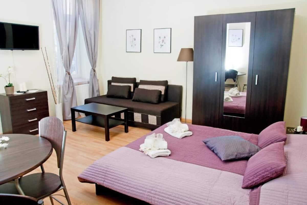 Quarto de hotel moderno com cama, sofá, mesa de jantar e televisão.