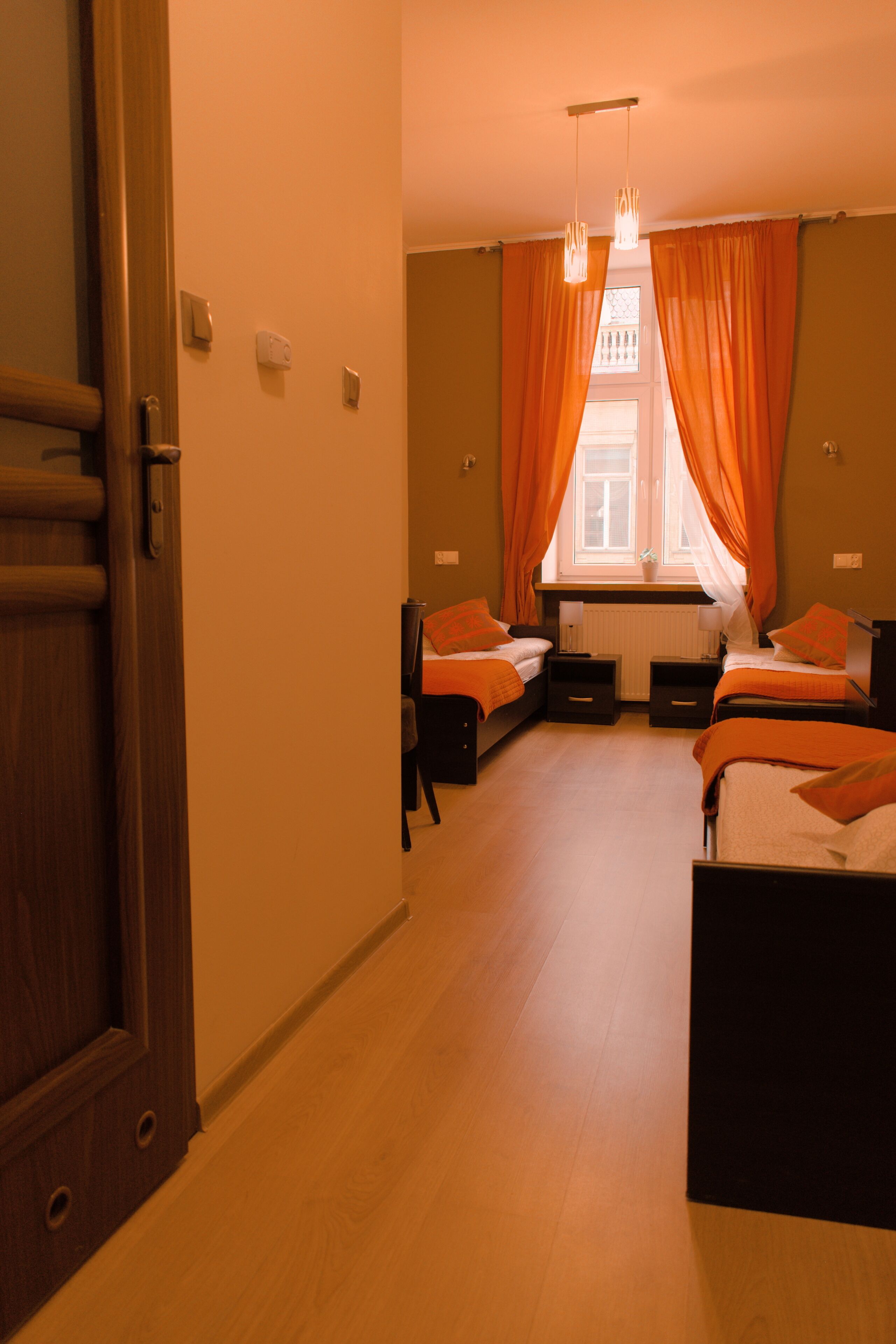 A hotel room with two beds, a window with curtains, a wooden floor, and a door.