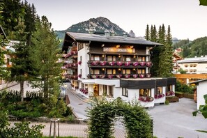 Un hotel de varios pisos con balcones decorados con flores, con montañas al fondo.