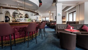 A bar area with a curved counter, multiple stools, and a seating area with sofas and a round table. - Hotel Dachstein (Filzmoos)