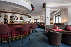 Una zona de bar con mostrador curvo, varios taburetes y un área de estar con sofás y una mesa redonda.
