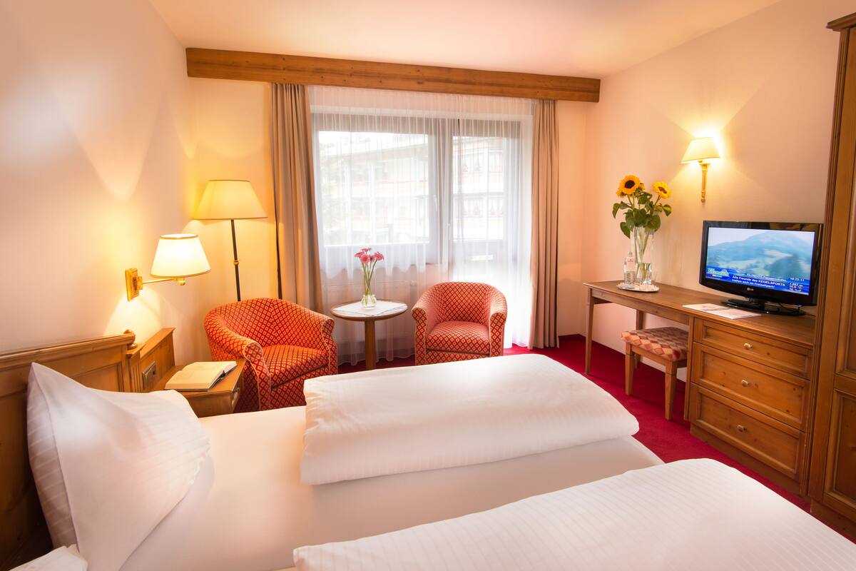 Une chambre d’hôtel avec deux lits, un bureau, une télévision, une chaise, une lampe et une fenêtre avec des rideaux.
