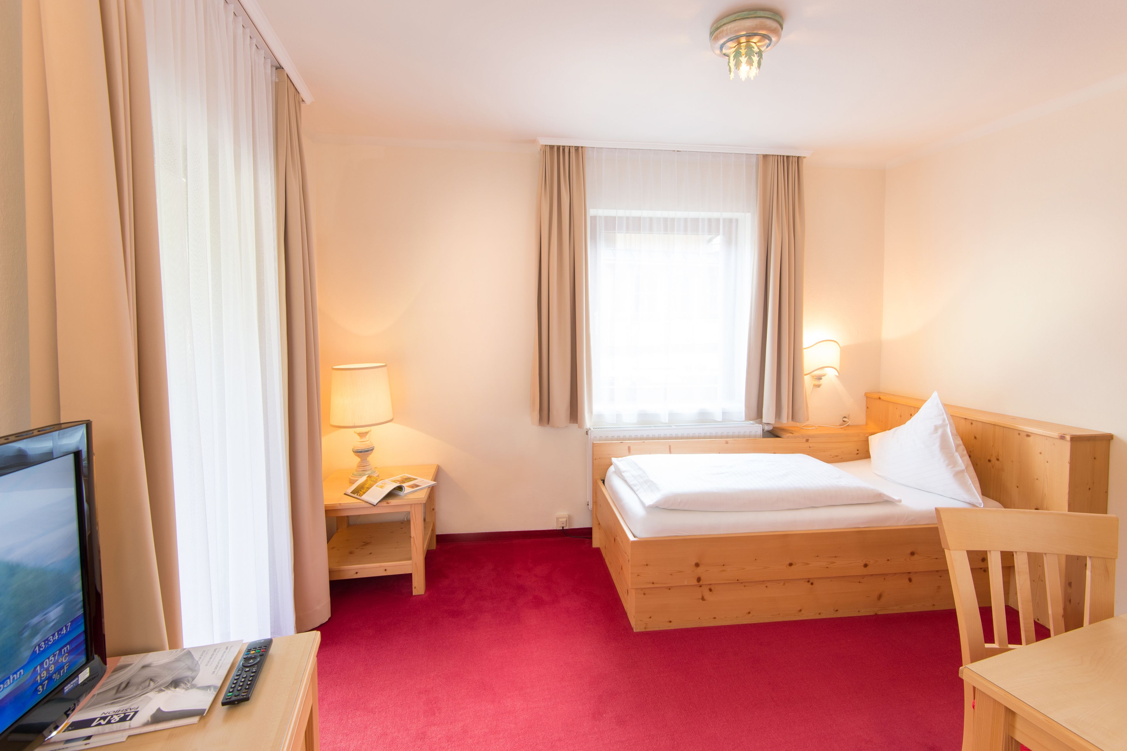 A hotel room with a wooden bed, a desk with a television, a lamp, and a window with curtains.