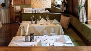 A dining area with a table set for four, a hanging light fixture, wooden walls, and a bench seating area. - Hotel Dachstein (Filzmoos)