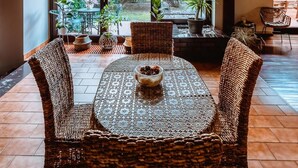 Un amplio patio con una mesa redonda y sillas de mimbre, ventanas grandes que ofrecen vistas al exterior y un techo de madera.