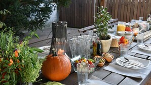 Mesa exterior dispuesta con diversos platos, un centro de mesa con calabaza y una botella de aceite de oliva.
