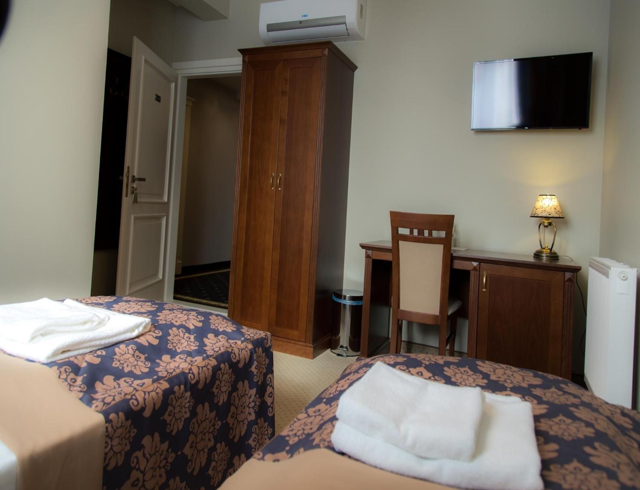 A hotel room with two beds, a desk, a chair, a TV, and a wardrobe.