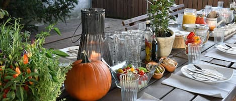 Mesa exterior dispuesta con diversos platos, un centro de mesa con calabaza y una botella de aceite de oliva.