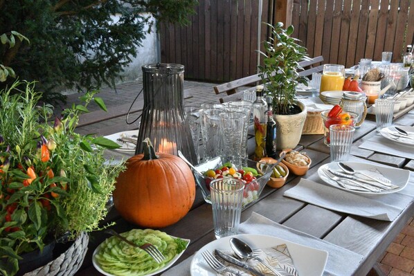 An outdoor dining table set with various dishes, a pumpkin centerpiece, and a bottle of olive oil.
