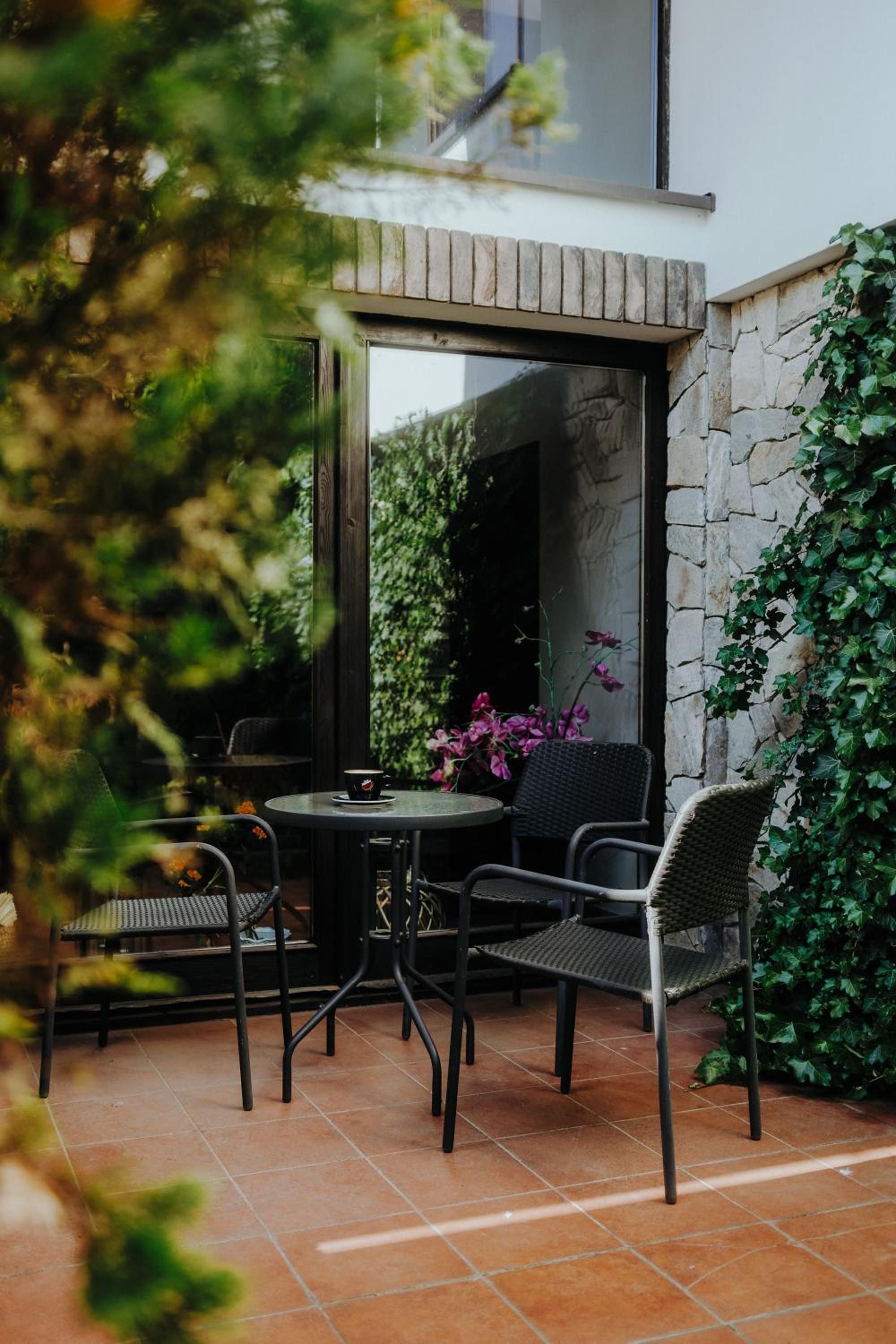 An outdoor patio with a round table and four chairs, surrounded by a stone wall and greenery.