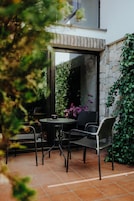 Un patio exterior con una mesa redonda y cuatro sillas, rodeado por un muro de piedra y follaje.