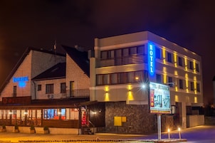 Hotel con fachada de piedra y estructura superior moderna, con señalización iluminada y entrada visible.