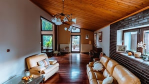 Un salón amplio con techo de madera, sofás de cuero, una mesa de centro de vidrio y vistas a través de un ventanal grande.