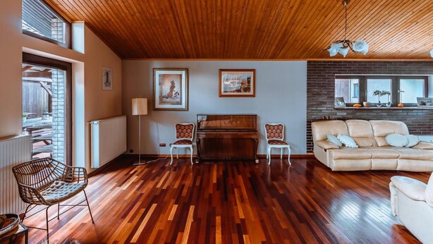 Amplia sala de estar con techo de madera, un piano, un sofá y un comedor con mesa y sillas.