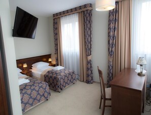 A hotel room with two beds, a desk, a chair, a TV, and curtains.