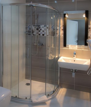 A modern bathroom with a glass-enclosed shower, a white sink, and a tiled wall.