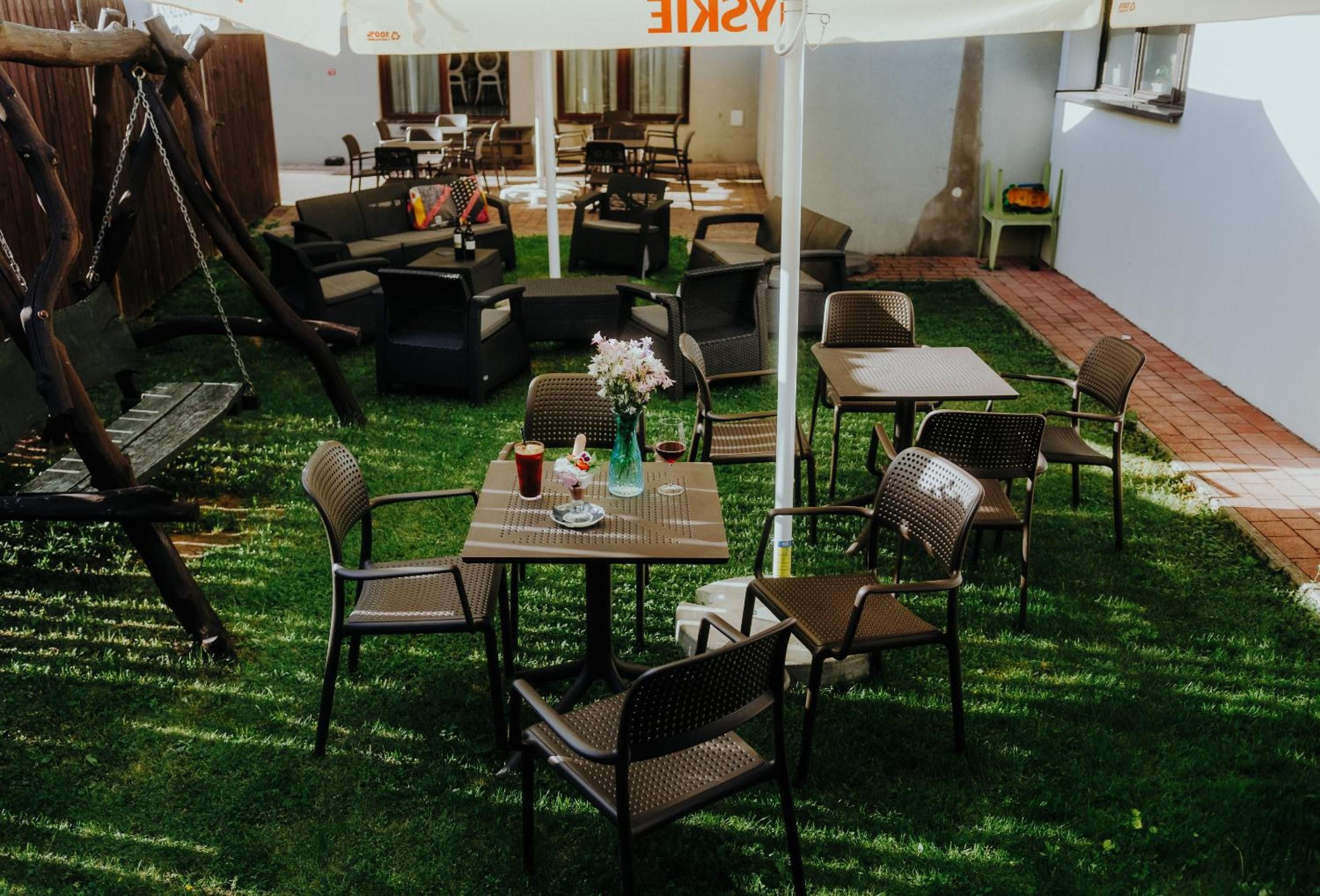 An outdoor seating area with tables and chairs, a swing set, and a covered umbrella.