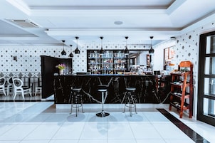 Zona de bar con mostrador de mármol negro, varios taburetes y una estantería bien surtida con diferentes botellas.
