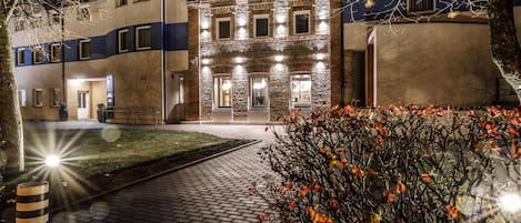 A building with a brick facade, multiple windows, and a paved entrance area.