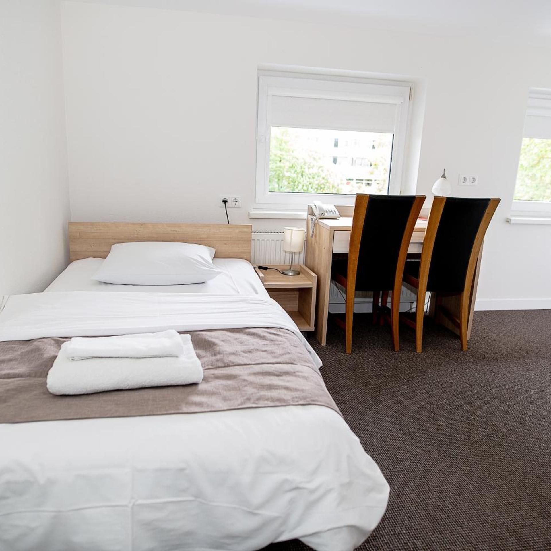 A hotel room with a double bed, a desk with a chair, and a window.