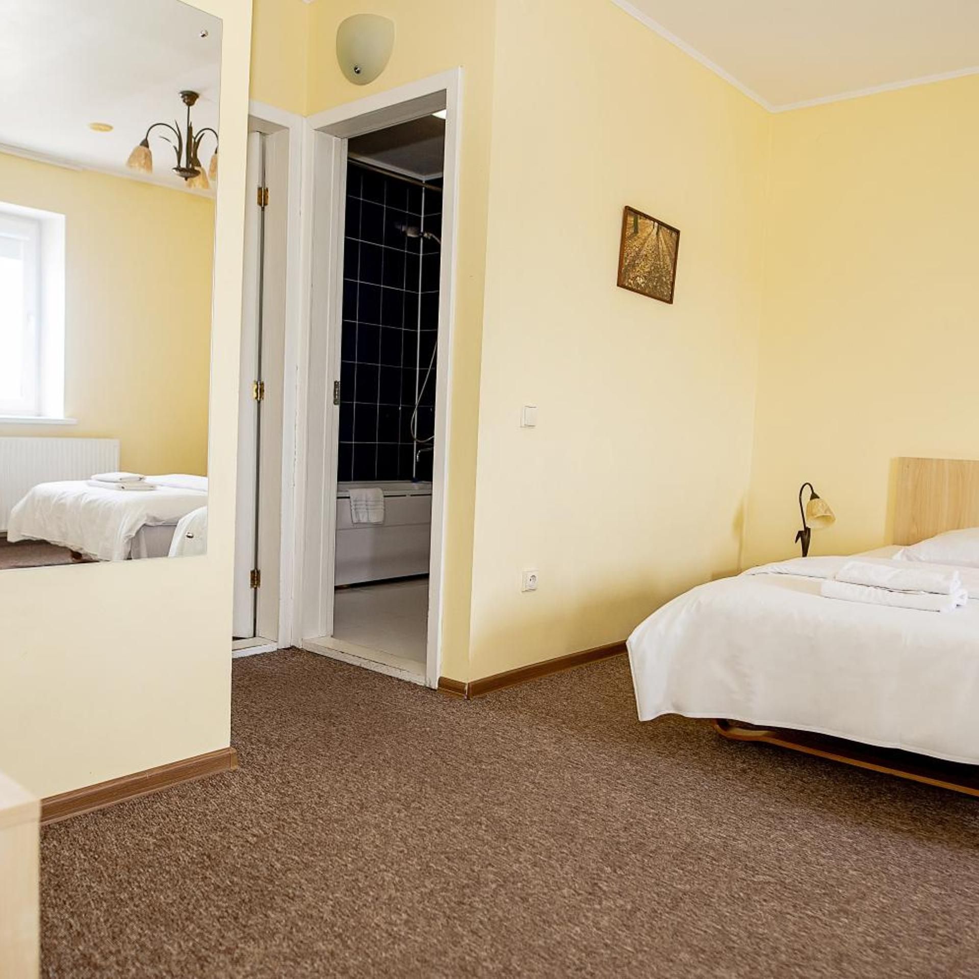 A hotel room with two beds, a bathroom with a shower, and a small painting on the wall.