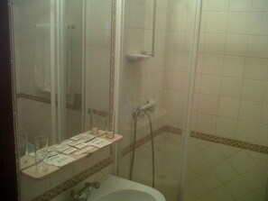 A bathroom with a shower, a sink, and a mirror. There is a shelf with papers and a glass. - Jardim (Elvas)