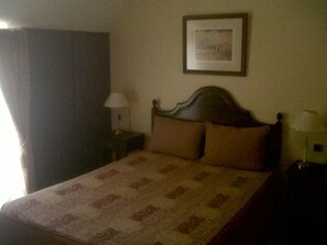 A neatly made bed with a patterned bedspread, a framed picture on the wall, and a lamp on a bedside table. - Jardim (Elvas)