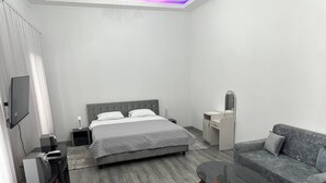 A modern hotel room with a bed, a sofa, a coffee table, a TV, and a desk with a lamp. - Hotel Lidia (Chisinau)