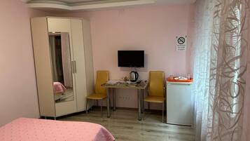 Una stanza con un letto, una televisione, una scrivania, due sedie, un armadio e un piccolo frigorifero.