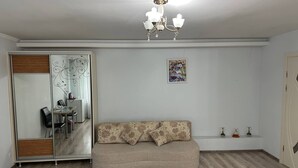 A room with a sofa, a chandelier, a dining area with chairs and a table, and a sliding door with a mirror. - Hotel Lidia (Chisinau)