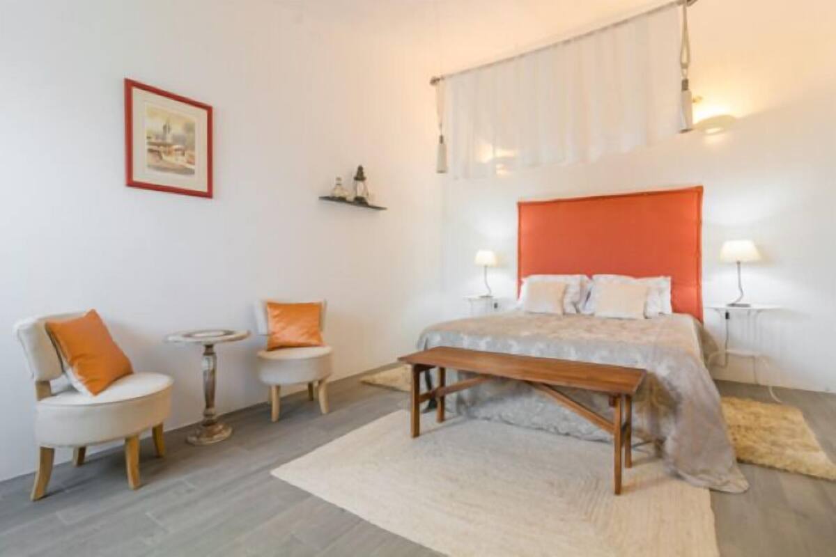 A bedroom with a large bed, two bedside tables, a chair, a small round table, and a picture on the wall.