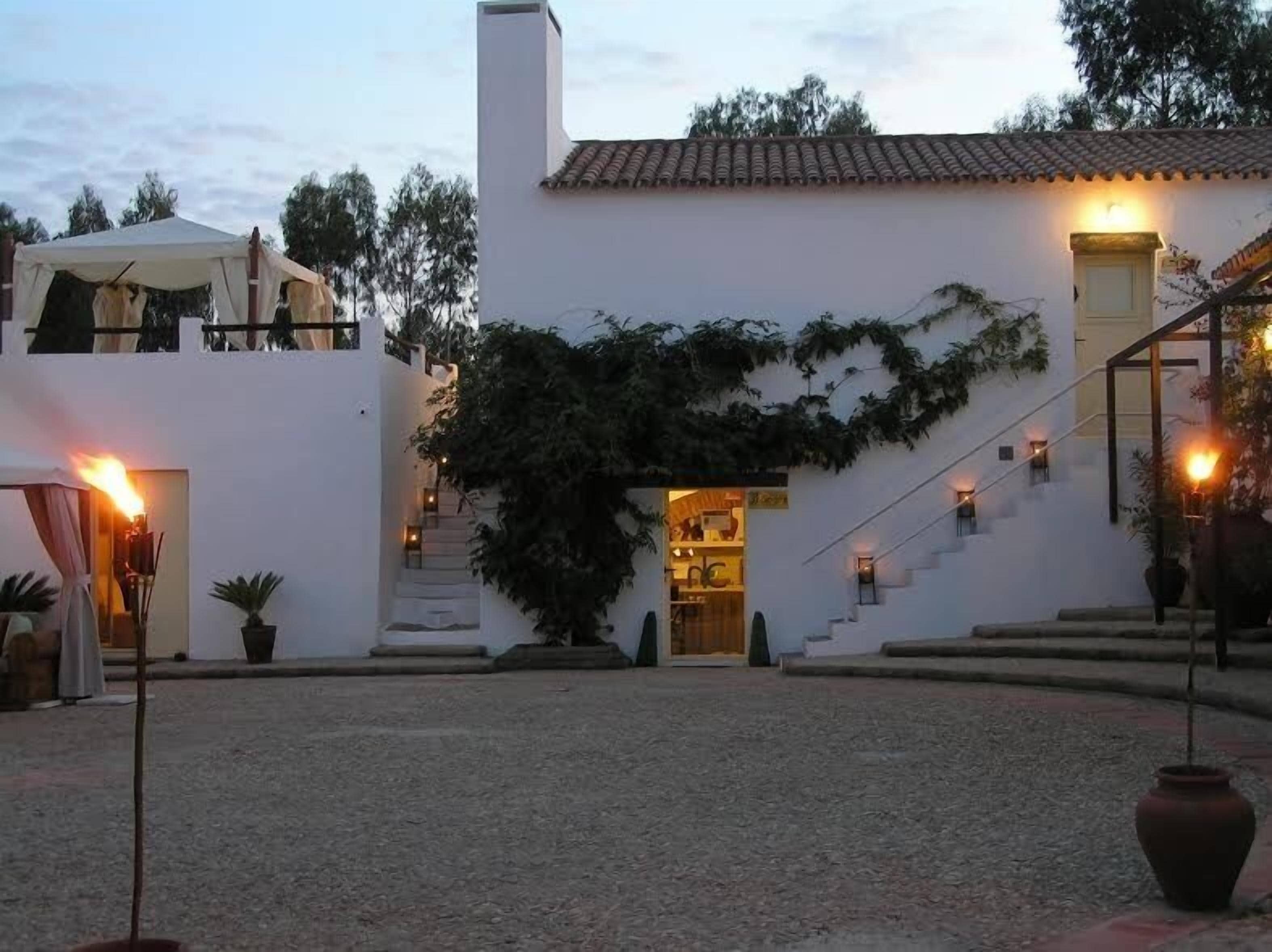 A white building with a tiled roof, a staircase leading to the entrance, and a covered area with a fire.