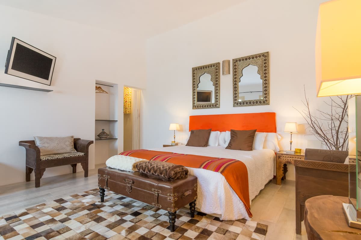 A hotel room with a large bed, two bedside tables, a chair, a suitcase, and a mirror on the wall.