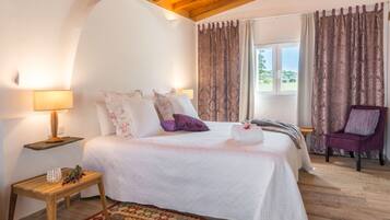 Un dormitorio con cama, mesita de noche, una silla y ventana con cortinas.