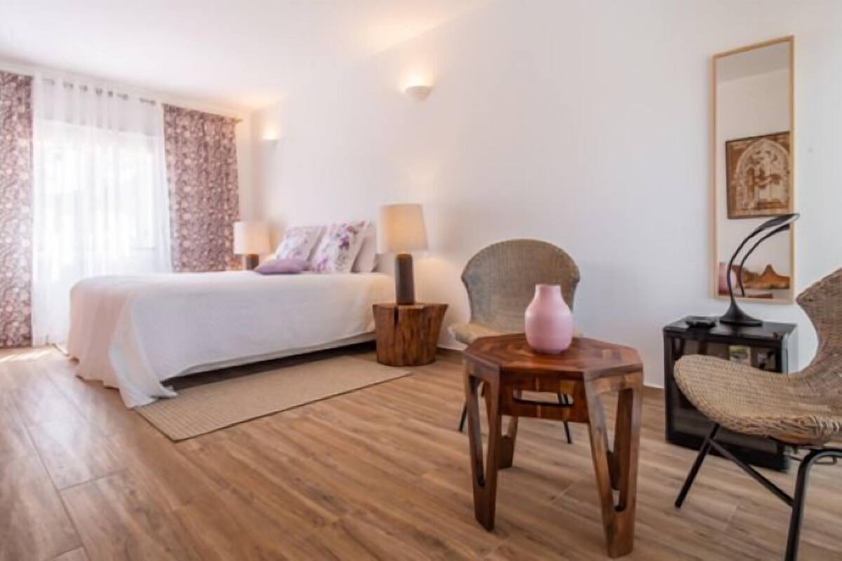 A bedroom with a bed, bedside tables, a chair, a lamp, and a vase on a wooden side table.