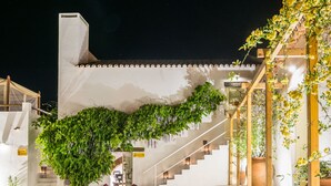 Um edifício branco com uma escadaria e uma trepadeira pendurada. Há uma placa com a inscrição