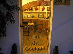 A doorway with a sign reading "Horta da Coutada." Inside, there is a reception desk, a computer, and a chair.