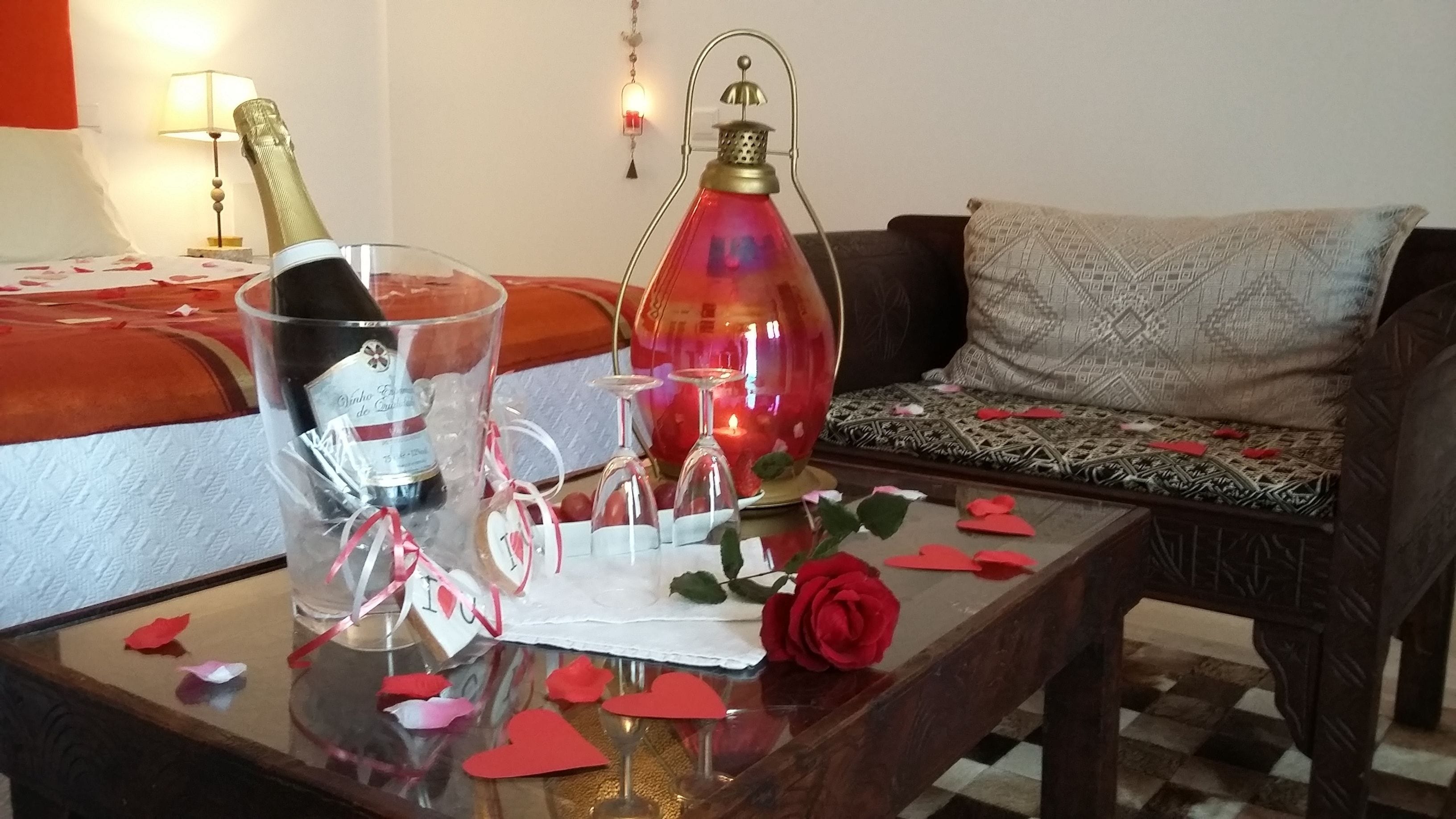 Une table en verre avec une bouteille de vin, une lanterne rouge et une rose.
