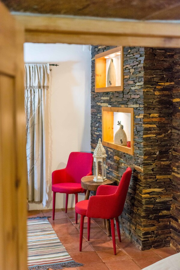 A cozy room with a stone wall, a wooden ceiling, a red chair, a wooden table, and a striped rug.