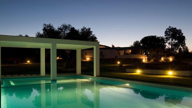 Piscina com design moderno, rodeada por uma área coberta e iluminada por iluminação ambiente.