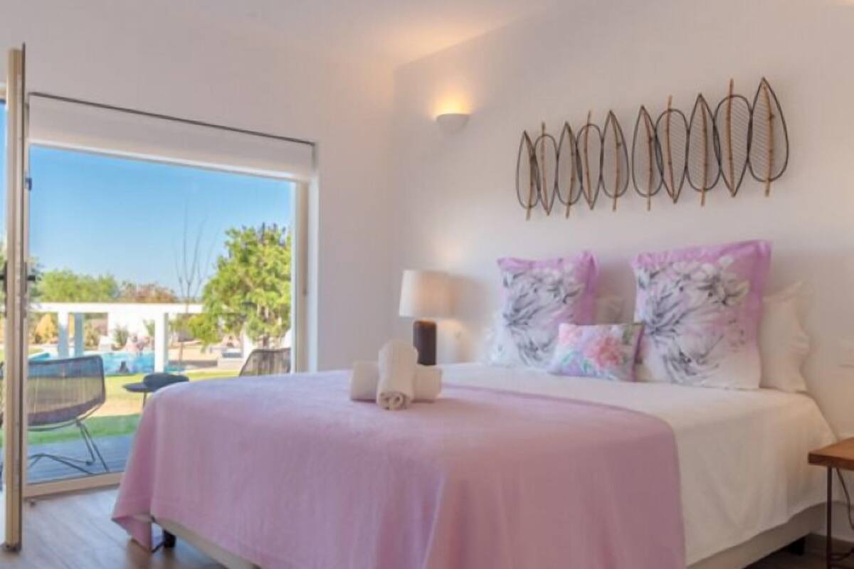 A bedroom with a bed, a bedside table, a lamp, and a view of the outdoors.