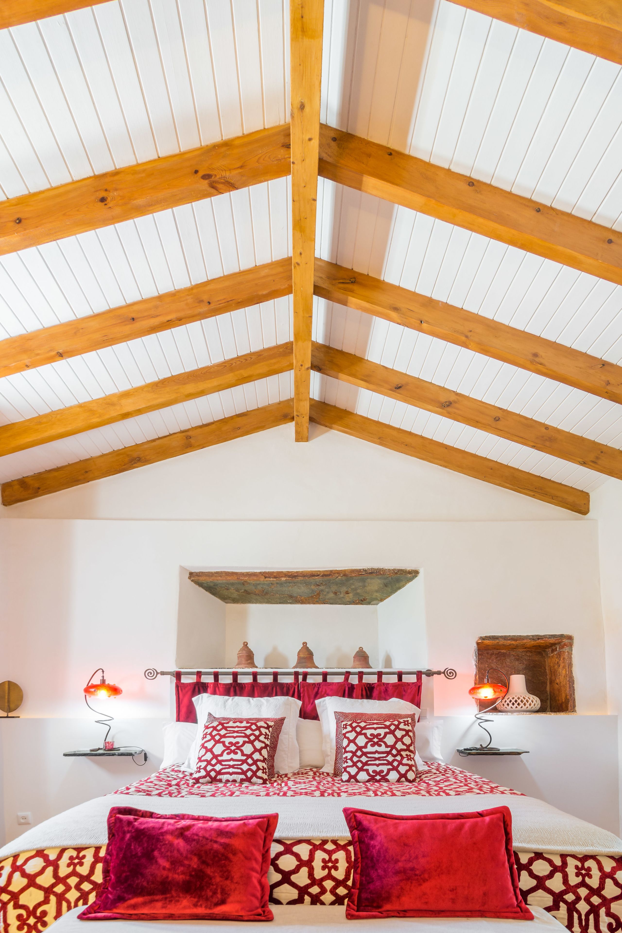 A bedroom with a high wooden ceiling, a bed with patterned bedding, and bedside lamps.
