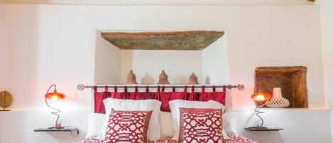 A bedroom with a high wooden ceiling, a bed with patterned bedding, and bedside lamps.