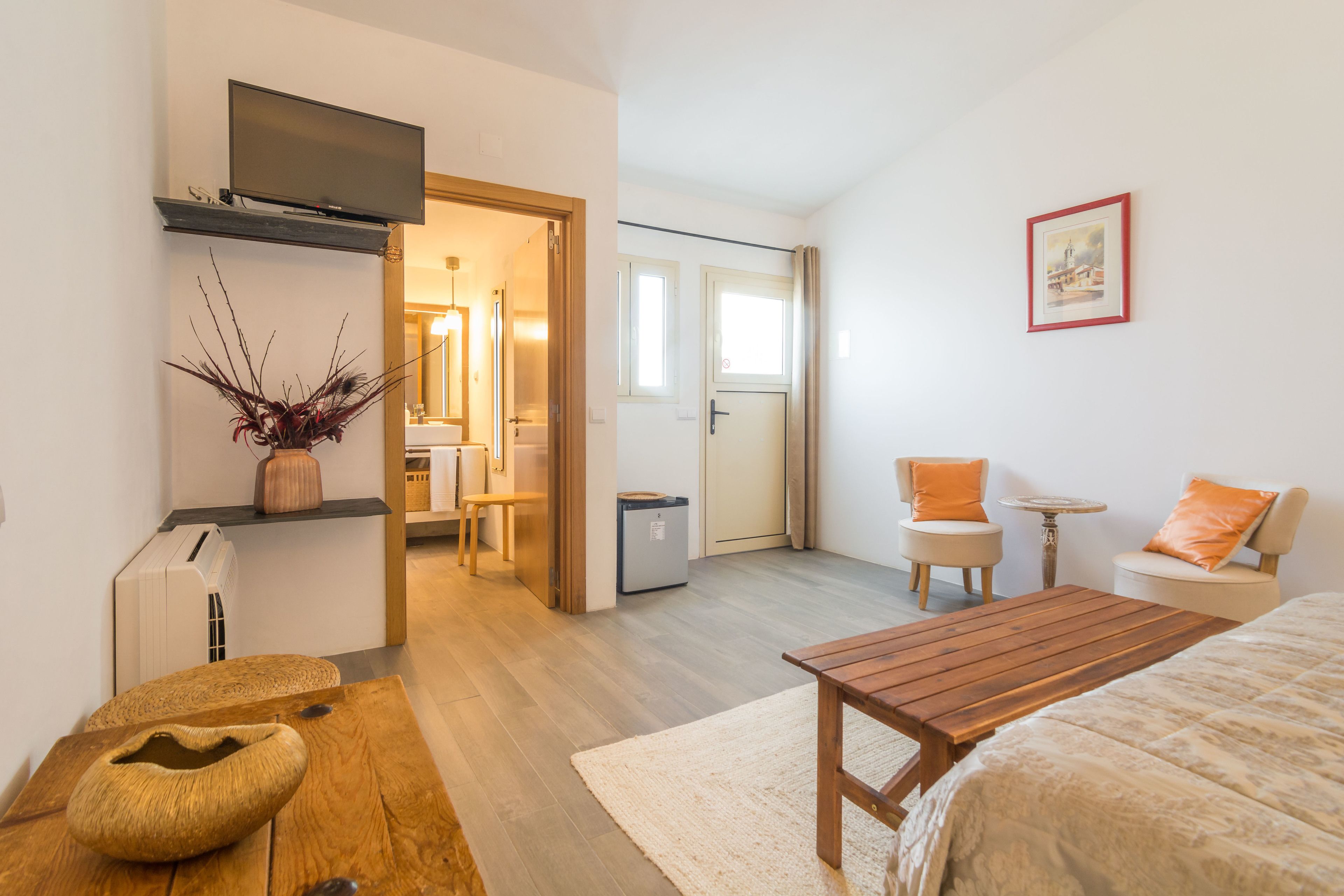 Een moderne hotelkamer met een houten bed, een klein houten tafeltje, een zithoek met twee stoelen, een aan de muur bevestigde televisie en een inlijsting foto.