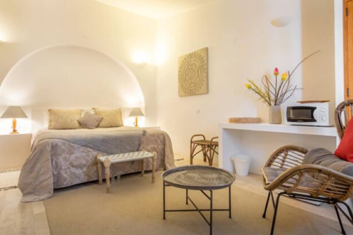 A bedroom with a bed, bedside tables, a small table, and wicker chairs.