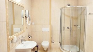 A bathroom with a glass-enclosed shower, a sink, a toilet, and a mirror with a telephone.