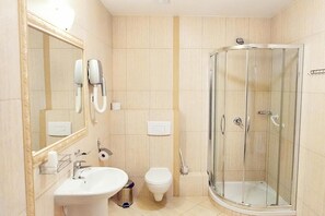 A bathroom with a glass-enclosed shower, a sink, a toilet, and a mirror with a telephone.