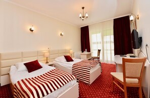 A hotel room with two beds, a desk, a chair, a television, and a window with curtains.
