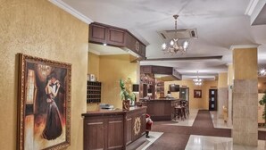 A hotel lobby with a reception desk, a large framed painting, and a chandelier.