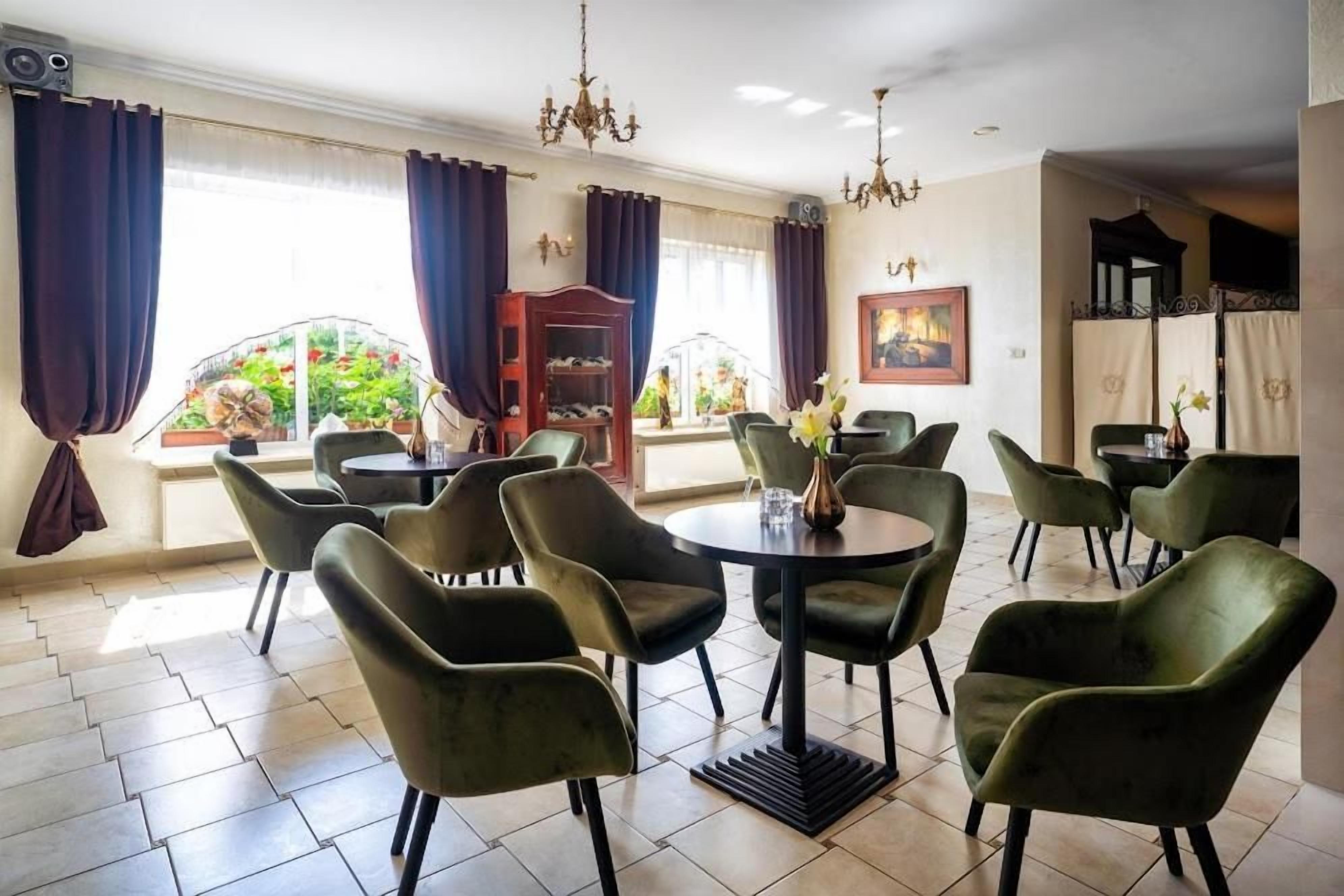 Un comedor con mesas redondas y sillas verdes, una araña y vistas a un jardín a través de grandes ventanales.